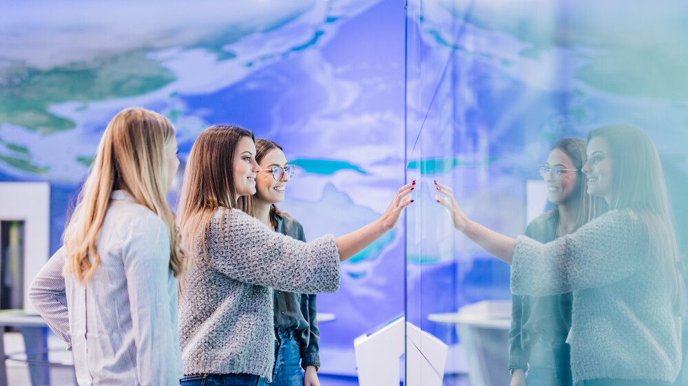 Drei Frauen stehen vor einem Ausstellungsmodul in der KLIMA ARENA.